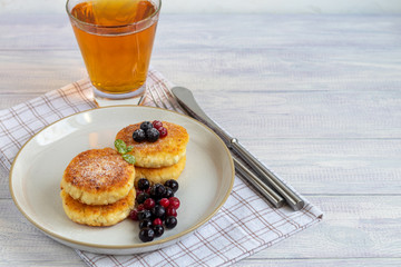 Homemade pancakes with cottage cheese on a white lantern with black currants and cranberries. Breakfast for the whole family. Healthy vegan food concept.