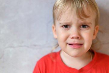Naklejka premium kid crying. the face of a cute little upset four year old baby boy in tears. children's grief. gray concrete wall background. space for text