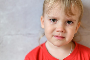 kid crying. the face of a cute little upset four year old baby boy in tears. children's grief. gray concrete wall background. space for text
