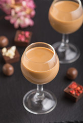 Sweet chocolate liqueur in glass on a black stone slate board. Side view, selective focus.