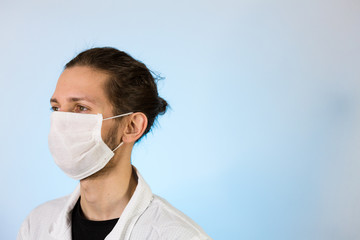 An adult male dressed in a white lab coat with a protective face mask on. Ready to work in a clean room or laboratory