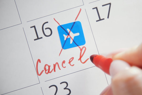 Close-up of unrecognizable person with red felt-tip pen cross out the note on calendar surface symbolizing scheduled flight. Cancelled flight due to border closure due to coronavirus pandemic
