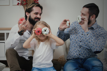 Male couple and little girl having fun with donuts