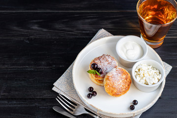 Homemade pancakes with cottage cheese on a dark lantern with black currants and cranberries. Breakfast for the whole family. Healthy vegan food concept.