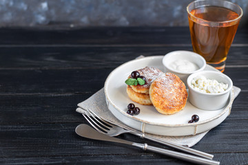 Homemade pancakes with cottage cheese on a dark lantern with black currants and cranberries. Breakfast for the whole family. Healthy vegan food concept.