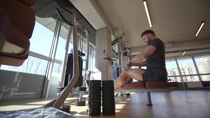 Handsome young man using seated row machine in the gym