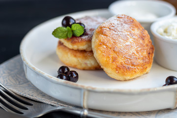 Homemade pancakes with cottage cheese on a dark lantern with black currants and cranberries. Breakfast for the whole family. Healthy vegan food concept.