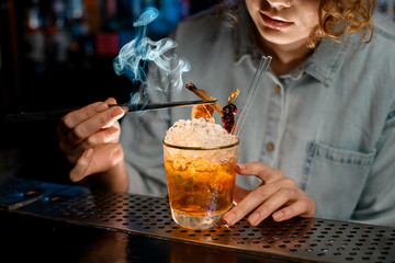 Close-up. Woman bartender decorates glass with cocktail by smoking stick