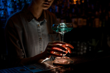 lady at dark bar holds beautiful glass of blue cocktail.
