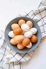 chicken eggs white and brown color in a gray plate on a checked kitchen towel on a white table....