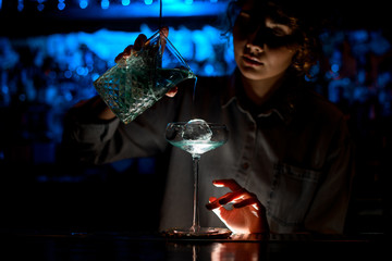 Woman at bar accurate pours cocktail into glass.