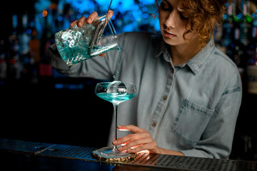 young woman bartender accurate pour cocktail into glass