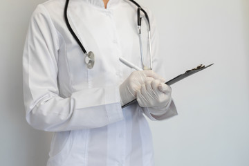 Clouse-up female doctor in a protective medical mask and gloves, writes the diagnosis to the...