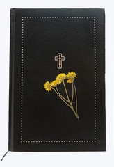 A small dried yellow flower lies on a large book with textured black leather cover