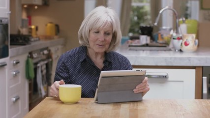 Senior woman reading on digital tablet on kitchen table