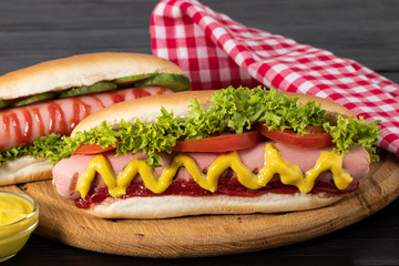 Hot dog with mustard, tomato and lettuce on wooden background