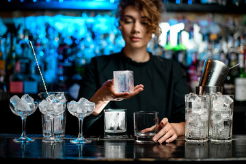 young bartender woman holds in hand large piece of ice. - obrazy, fototapety, plakaty