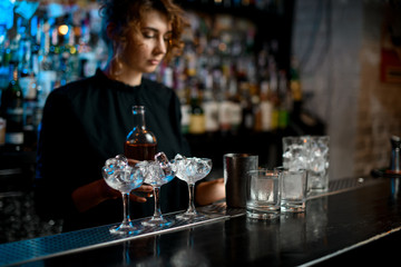 young woman at bar holds bottle with drink in her hand.