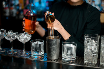 Close-up barman masterfully pours drink into metal glass using jigger