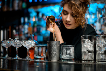 barman woman masterfully pours drink into metal glass to make negroni coctail.