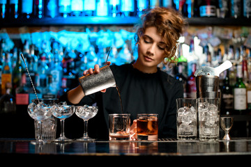 Young woman barman preparing cocktail and pouring it into glass.