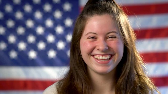 Closeup portrait of teen girl looking at camera and giggling and laughing with American flag background.