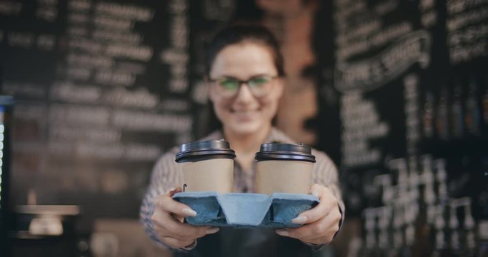 Female barista serving two paper cups of coffee with smile