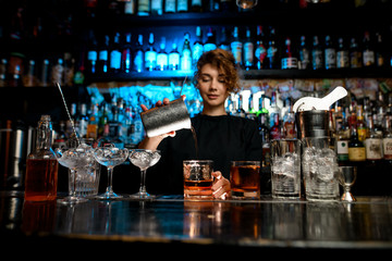 Young lady at bar pours cocktail into glass.