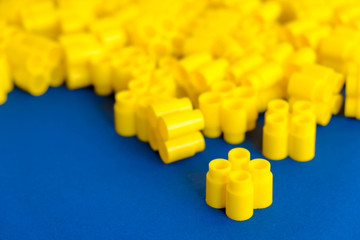 Yellow plastic building blocks on a blue background. Pieces and elements of constructor. Parts of bright small spare parts for toys. Top view. Copy, empty space for text