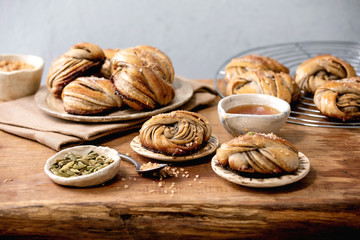 Traditional Swedish cardamom sweet buns Kanelbulle on plate, ingredients in ceramic bowl above on wooden table.