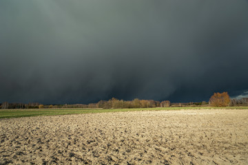 Dark dangerous cloud coming over a plowed field, forest on the horizon,