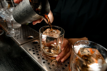 Close-up bartender pours negroni cocktail into glass on bar counter.