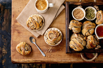 Traditional Swedish cardamom sweet buns Kanelbulle in wooden tray, cup of coffee, ingredients in...