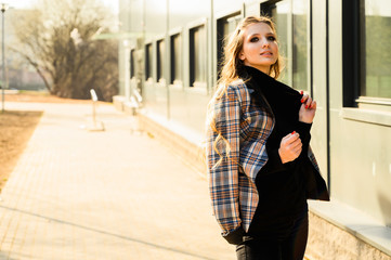 Obraz premium Portrait of a pretty beautiful young girl with long hair with a smile in the city against the background of the wall of a business building. Photo taken in sunny weather outdoors in spring.