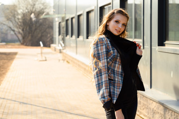 Portrait of a pretty beautiful young girl with long hair with a smile in the city against the background of the wall of a business building. Photo taken in sunny weather outdoors in spring.