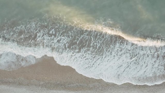 Beautiful HD tropical beach aerial - a bird's eye view of sea waves crashing against an empty beach from above