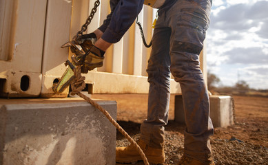 Safe workplace trained competent rigger wearing a safety hand protection glove clipping crane hook into pig ears lifting lug which it attached on corner of while containers prior lifted 