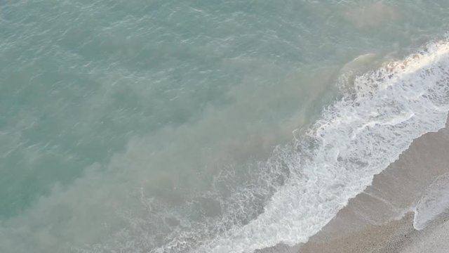 Aerial view of a transparent blue sea with beautiful waves at sunny day in summer. Top view from flying drone.