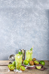 Summer cold drink and beverages recipes. Kiwi Lime Mojito cocktail or non-allcohol mocktail with limes, mint and sliced kiwi fruits on wooden background copy space