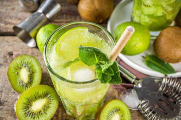 Summer cold drink and beverages recipes. Kiwi Lime Mojito cocktail or non-allcohol mocktail with limes, mint and sliced kiwi fruits on wooden background copy space