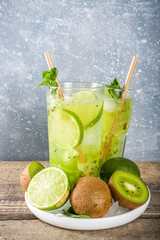 Summer cold drink and beverages recipes. Kiwi Lime Mojito cocktail or non-allcohol mocktail with limes, mint and sliced kiwi fruits on wooden background copy space