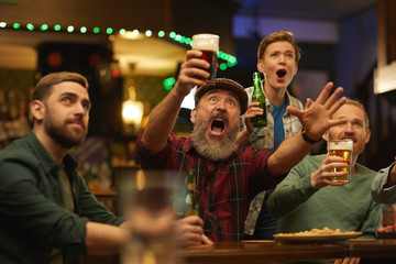 Excited people drinking beer and screaming they cheering for the football team in sport bar