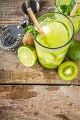 Summer cold drink and beverages recipes. Kiwi Lime Mojito cocktail or non-allcohol mocktail with limes, mint and sliced kiwi fruits on wooden background copy space