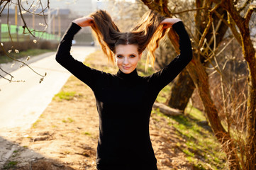 Portrait of a pretty young girl with long hair with a smile on the background of road trees in the...