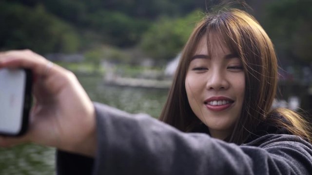 Lifestyle shot of beautiful asian woman from Taiwan playing with her hair and posing while taking picture selfies in Dahu park in the city Taipei next it's little lake in slow motion 1080p