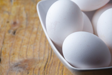 Aerial view of white eggs in a white bowl, with selective focus, on rustic wooden table in horizontal, with copy space