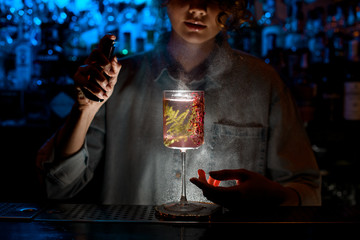 illuminated decorated glass with pink drink stands at dark bar.