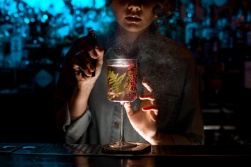 Woman bartender sprinkles on glass with fresh pink cocktail.