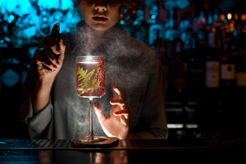 Woman bartender actively sprinkles on glass with fresh pink cocktail.
