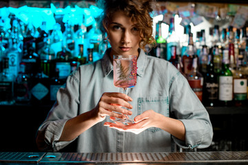 Pretty lady barman carefully holds glass in her hands.
